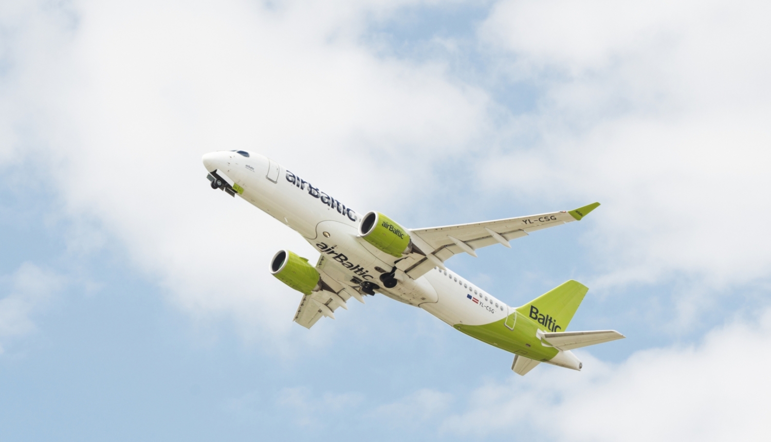 airbaltic lidmašīna pacēlusies gaisā dienas laikā, fonā daži mākoņi