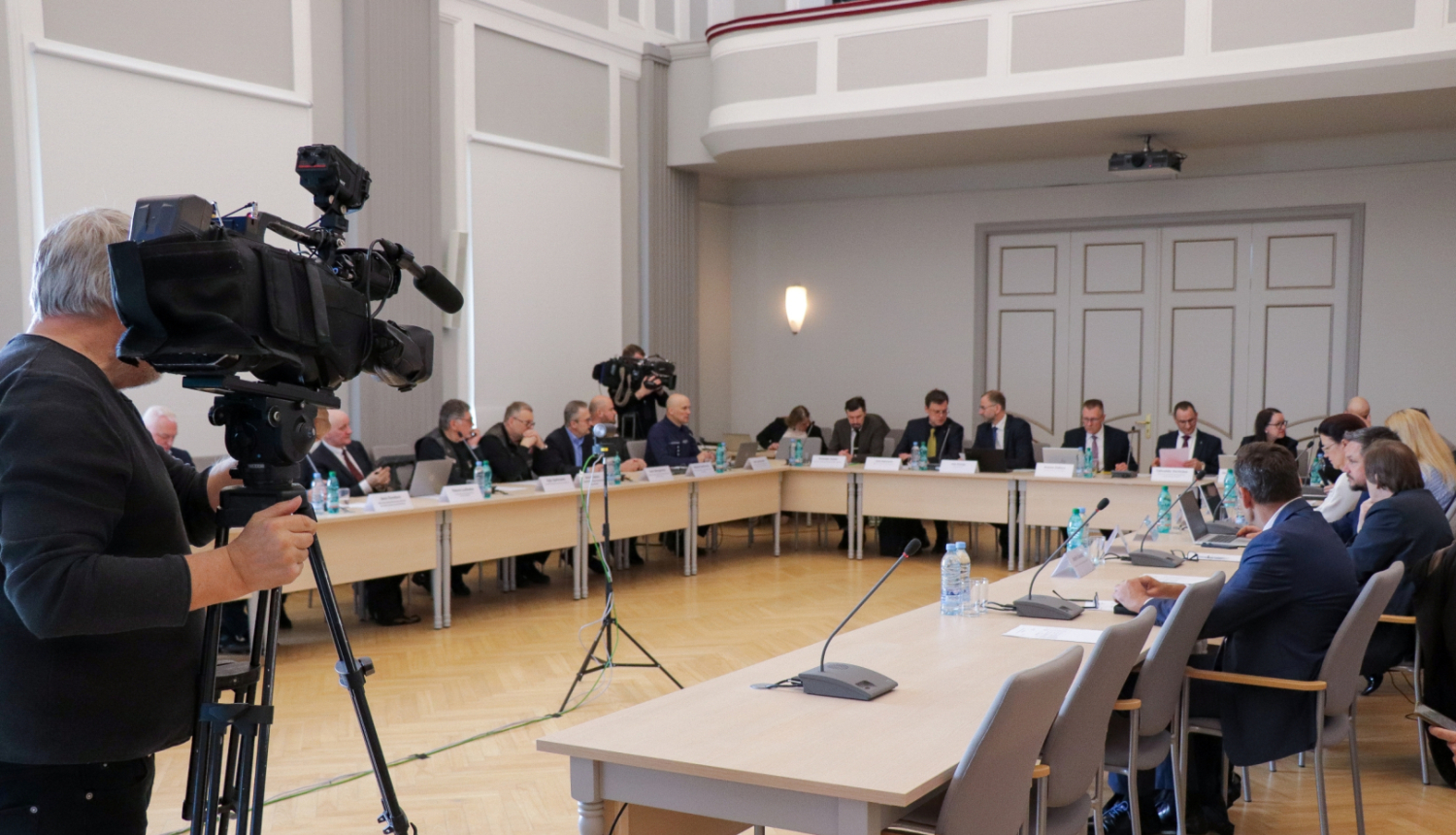 CSDP sēdes kopbilde,kur visi dalībnieki sēž pie galdiem. Tos filmē operators no televīzijas