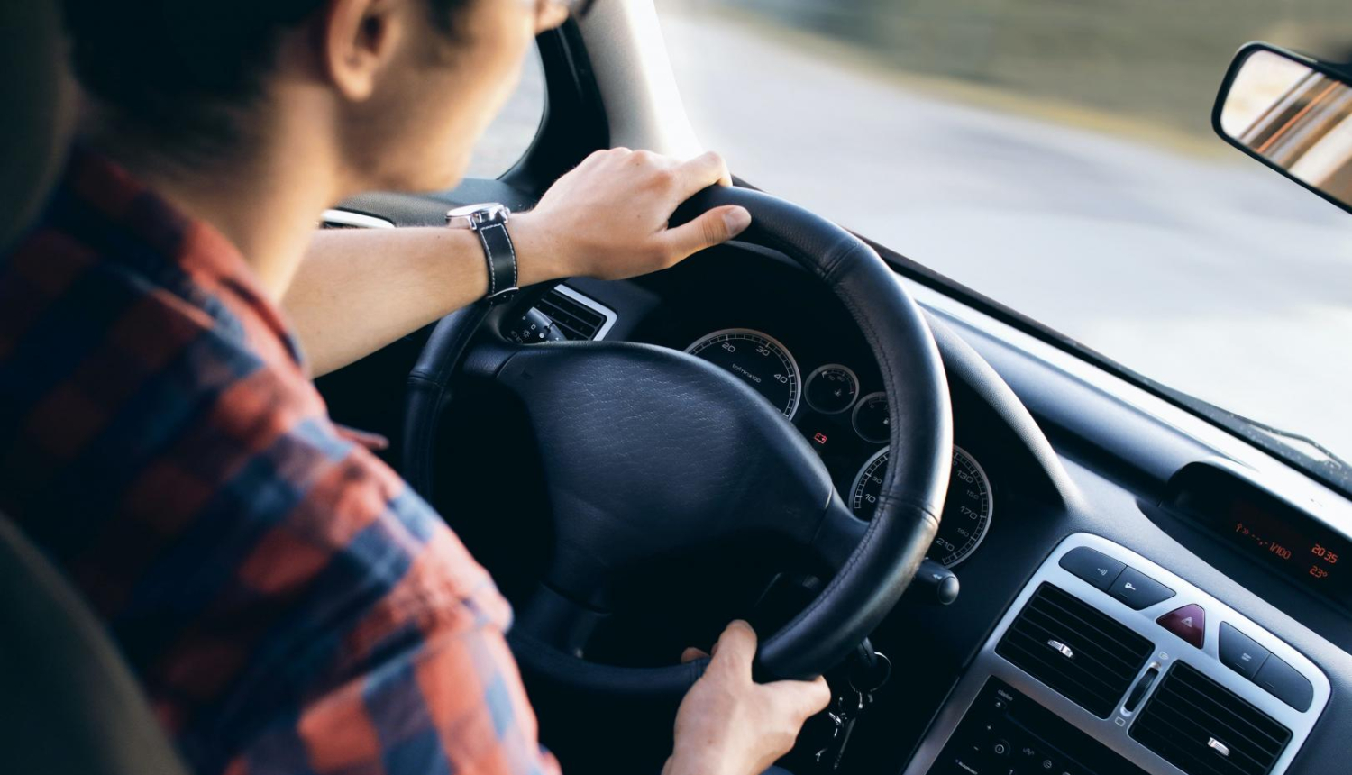 vīrietis rūtainā kreklā pie vieglā auto stūres