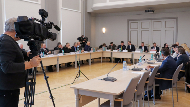 CSDP sēdes kopbilde,kur visi dalībnieki sēž pie galdiem. Tos filmē operators no televīzijas