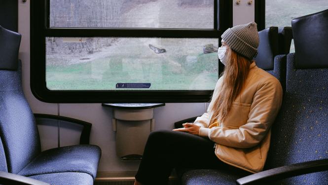 sieviete ar baltu sejas masku skatās pa vilciena logu