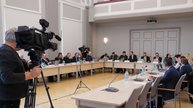 CSDP sēdes kopbilde,kur visi dalībnieki sēž pie galdiem. Tos filmē operators no televīzijas