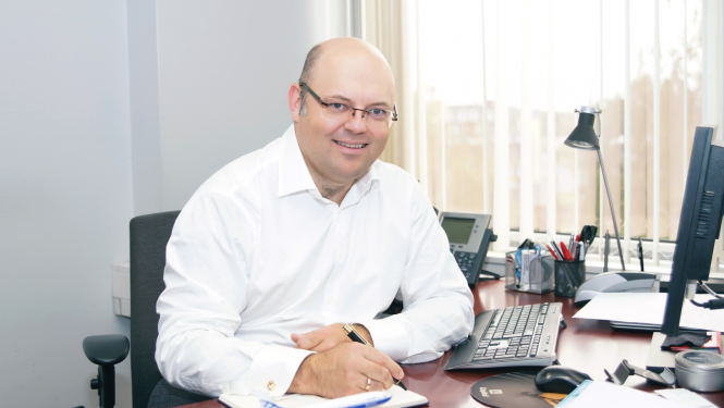 vīrietis pie biroja galda paraksta dokumentu