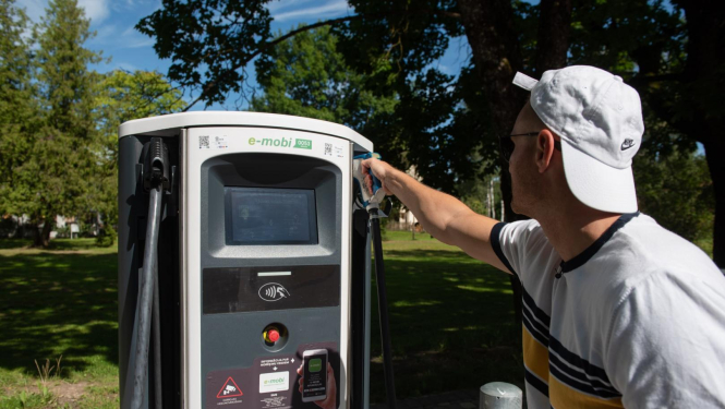 vīrietis pie elektroauto uzlādes stacijas vasarā