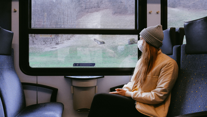 sieviete ar baltu sejas masku skatās pa vilciena logu