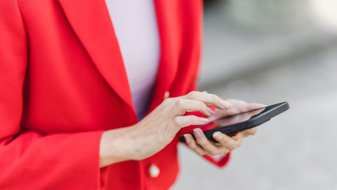 sieviete sarkanā žaketē tur rokās viedtālruni