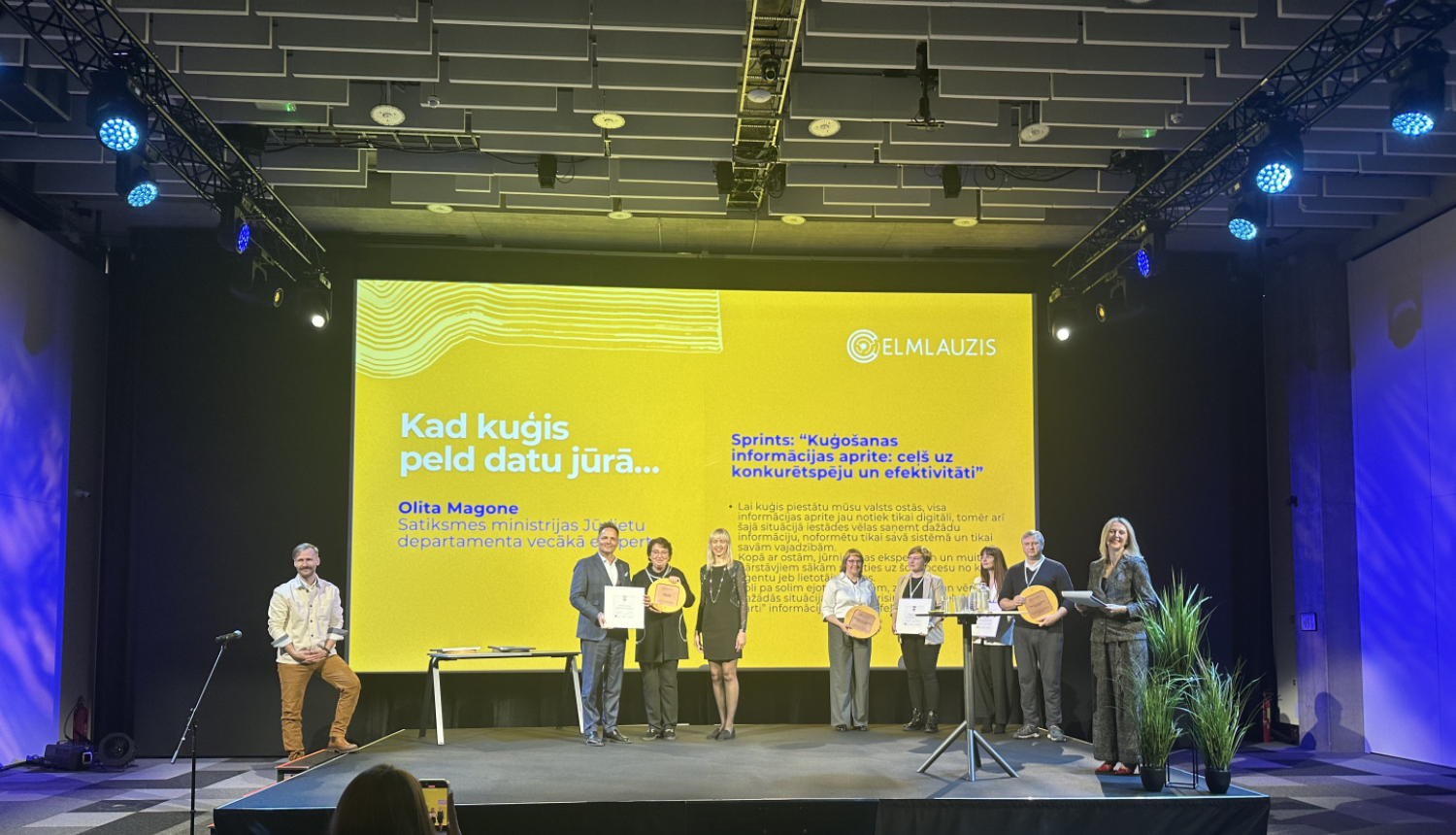 Satiksmes ministrijas pārstāvji saņem balvu uz pasākuma skatuves