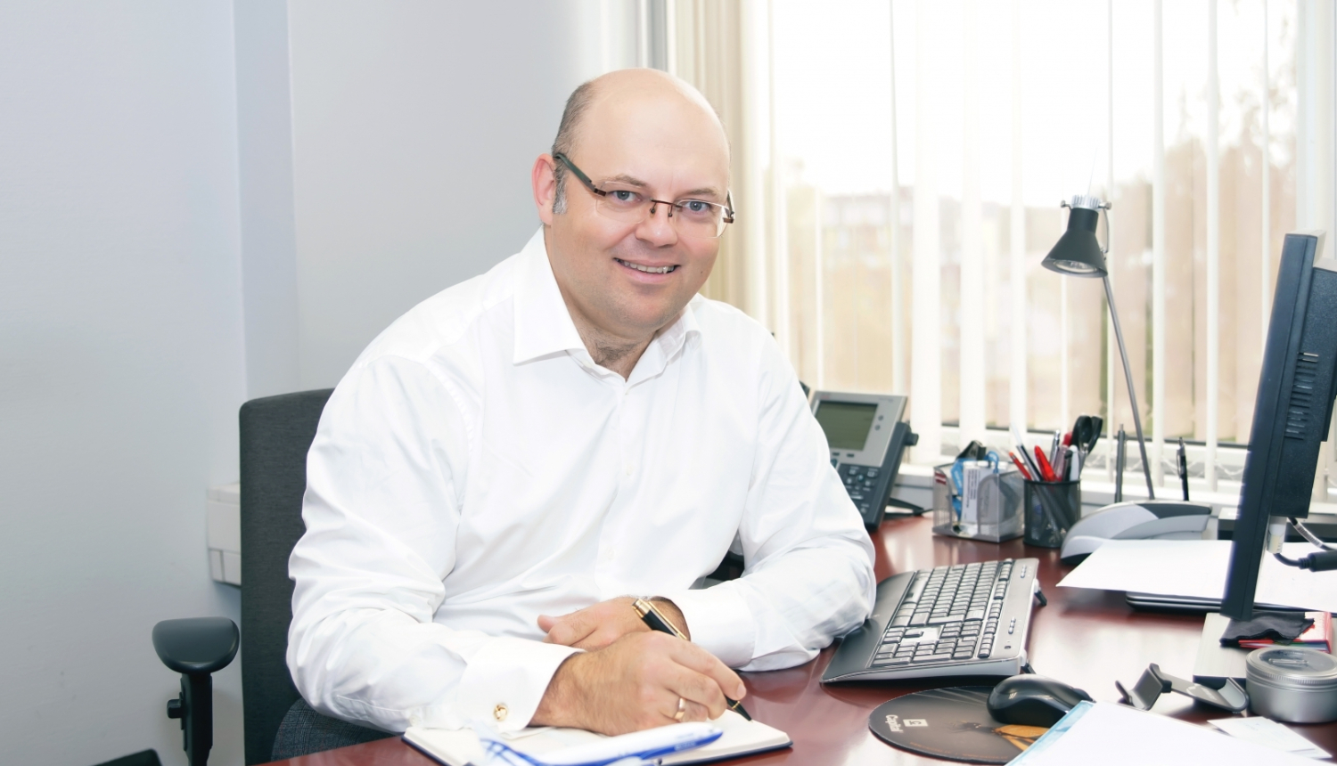 vīrietis pie biroja galda paraksta dokumentu