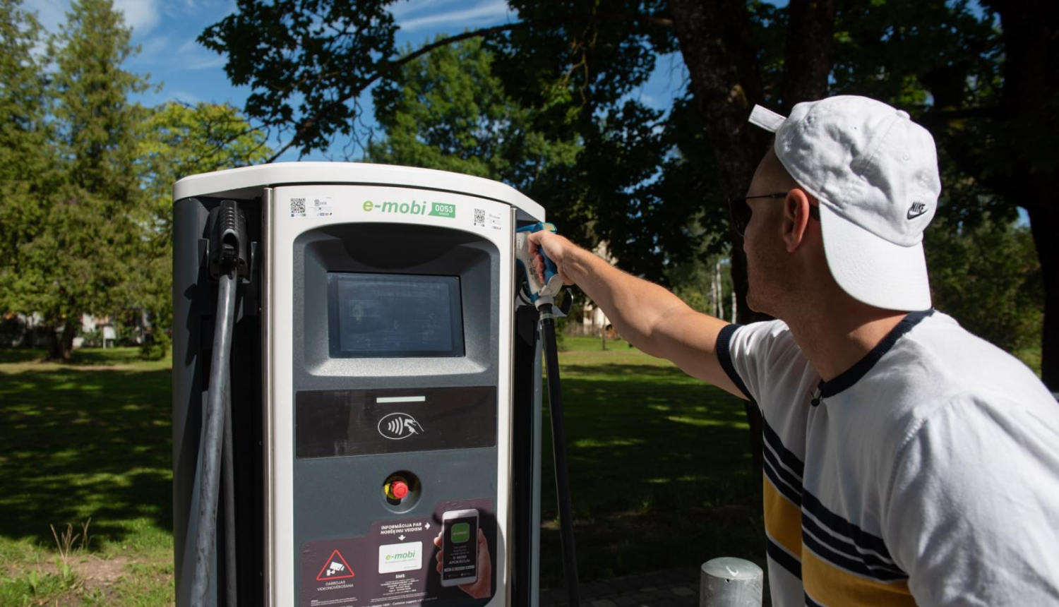 vīrietis pie elektroauto uzlādes stacijas vasarā