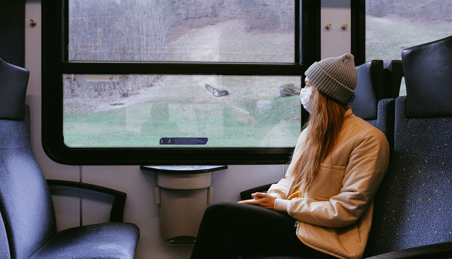 sieviete ar baltu sejas masku skatās pa vilciena logu