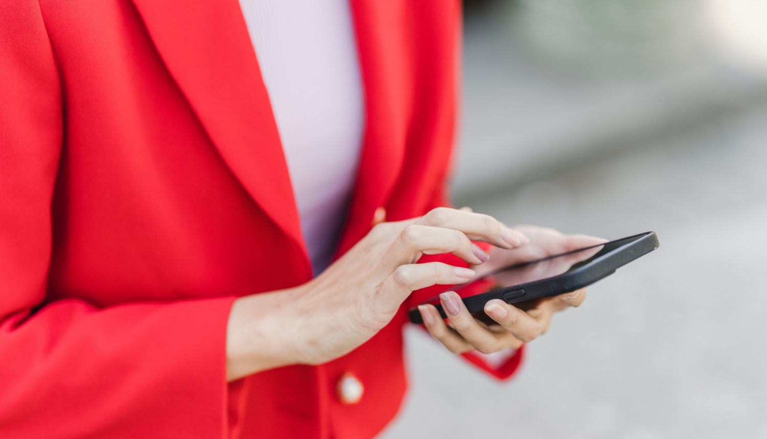 sieviete sarkanā žaketē tur rokās viedtālruni