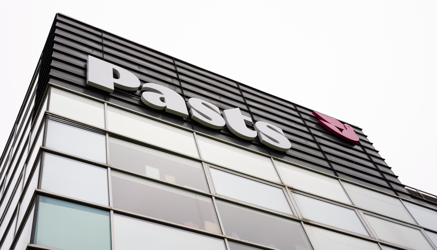 Nofotografēta Pasta ēkas daļa. Redzama logu siena un uz tās PASTS logo.