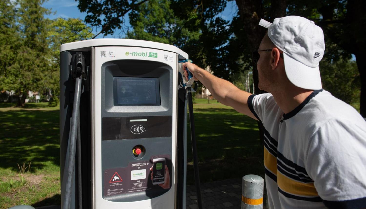 vīrietis pie elektroauto uzlādes stacijas vasarā