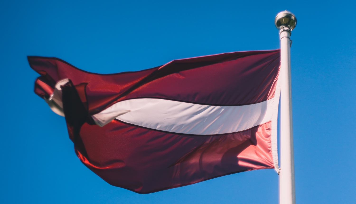 Latvijas karogs uz zilu debesu fona